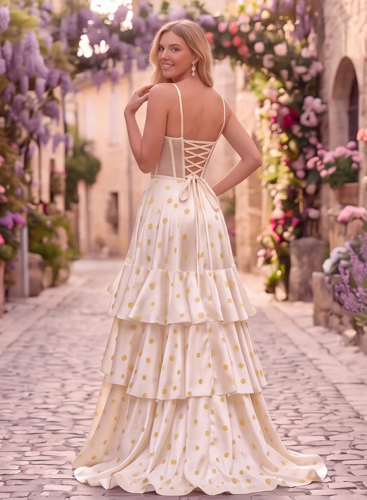 Back view of an ivory polka dot prom gown featuring a lace-up corset back, thin straps and a flowing tiered skirt.